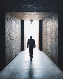 Rear view full length of man walking in passage amidst walls