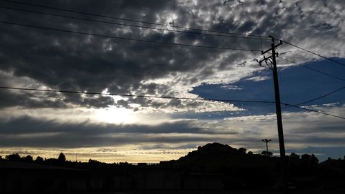 Low angle view of electricity pylon against cloudy sky