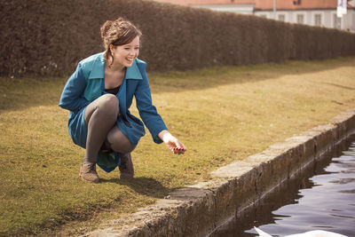 Beautiful happy woman crouching by lake on sunny day