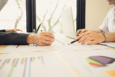 Cropped image of business people discussing over graph at desk in office