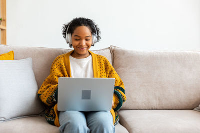 Young woman using laptop while sitting on sofa at home