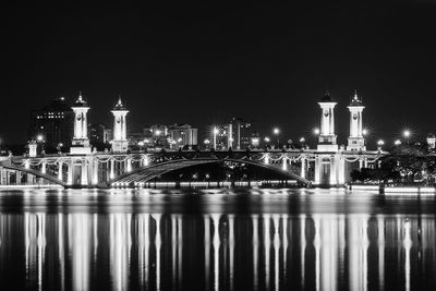 Illuminated arch bridge reflecting on river against sky at night