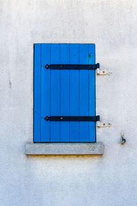 Old window with wooden blue painted shutter on white painted wall.