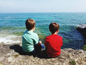 Rear view of people sitting on rock by sea