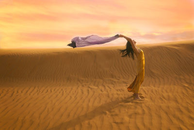 Woman in yellow dress playing with the wind in the desert v