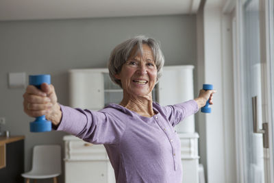 Portrait of happy senior woman doing fitness exercise with dumbbells at home