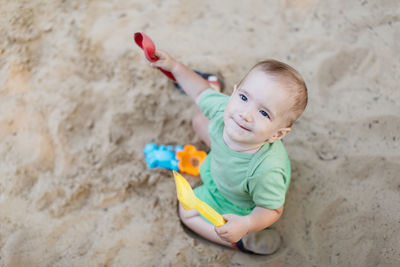 High angle view of cute baby boy looking up while playing on sand at beach