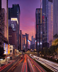 Light trails on road amidst buildings against sky at night