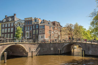 Bridge over river by buildings against sky