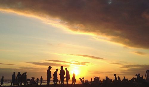 Silhouette people at beach against sky during sunset