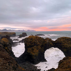 Rocks on beach against sky during sunset