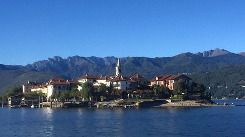 Buildings in front of river against clear blue sky