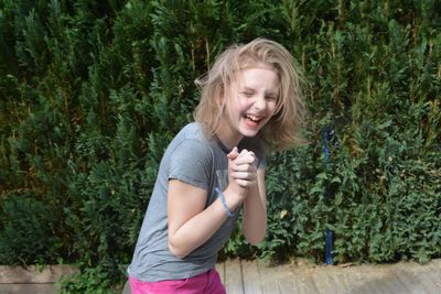 Happy girl laughing with hands clasped against plants