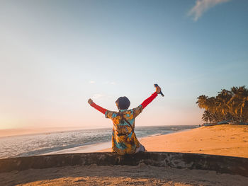 Rear view of woman at beach against sky during sunset