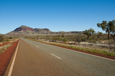 Road leading towards mountains against clear blue sky