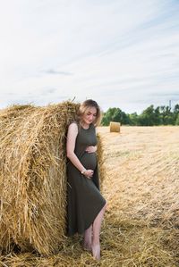 Pregnant woman standing against bale on field