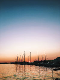 Silhouette sailboats moored at harbor against clear sky during sunset