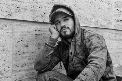 Portrait of young man sitting against wall