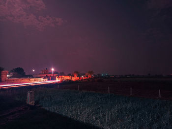 Illuminated buildings on field against sky at night