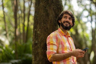 Young man with smartphone at day time with a green park in the background. mobile phone, technology,