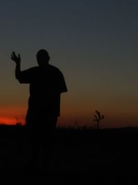 Silhouette man standing on field against sky during sunset