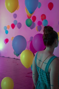 Rear view of woman with colorful balloons against wall