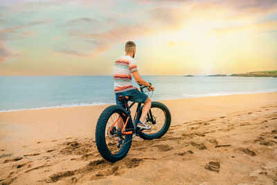 Unrecognizable man from behind looking at the sea riding a fat bike on the beach