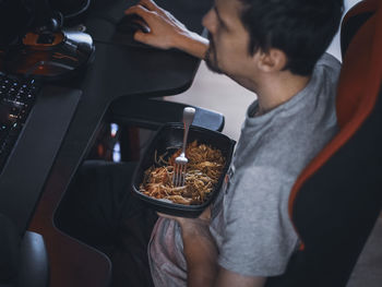 Young caucasian guy gamer holding a black container with wok food during lunch break