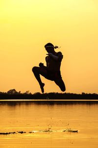 Silhouette man jumping against orange sky