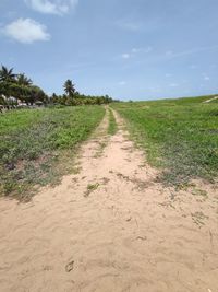 Dirt road on field against sky