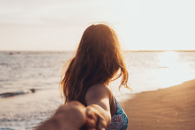 Rear view of woman sitting at beach against sky during sunset