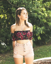 Thoughtful teenage girl looking away while standing against trees in park