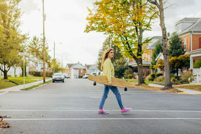 Girl crossing street in small town while holding a longboard with flowing hair