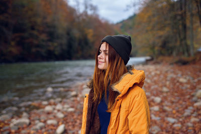 Young woman looking away while standing on tree during autumn