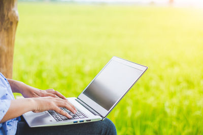 Midsection of woman using laptop while sitting against plants
