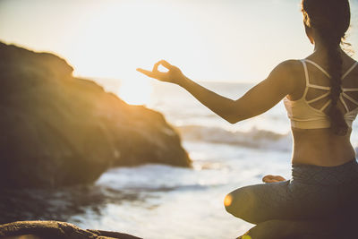 Woman standing on rock at beach against sky during sunset