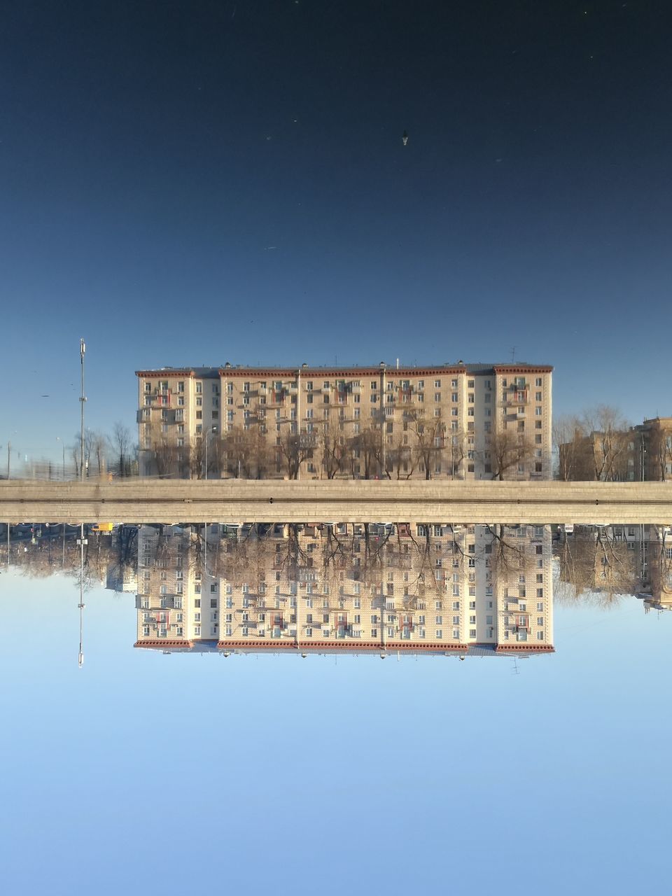 REFLECTION OF BUILT STRUCTURE IN CALM LAKE AGAINST CLEAR BLUE SKY