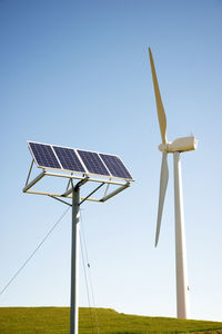 Wind turbine and solar panels on field against clear sky