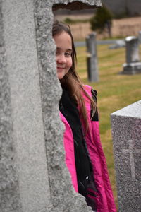 Portrait of smiling girl standing by cross in cemetery