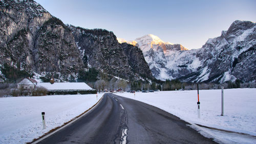 Empty road by snowcapped mountains against sky