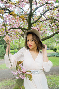 Beautiful young woman standing by tree in park