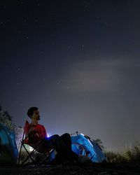 Man sitting on chair against sky at night