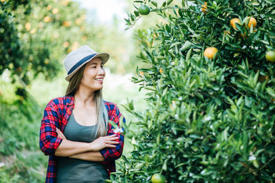 Smiling woman standing by orange tree in orchard