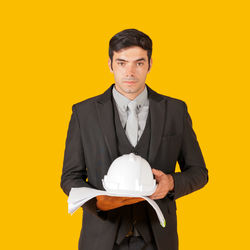 Portrait of young man standing against yellow background