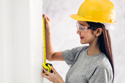 Young woman working at construction site against wall