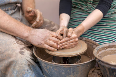 Midsection of man and woman molding a shape on pottery wheel