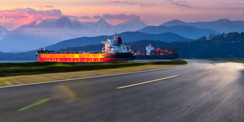 Scenic view of road by mountains against sky during sunset