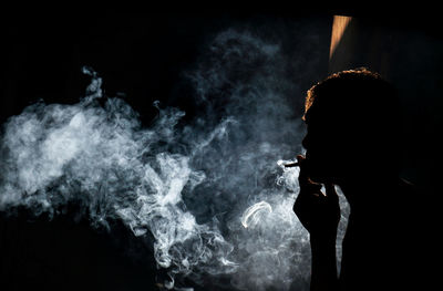 Side view of man smoking cigarette against black background