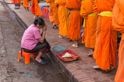 Side view of woman with hands clasped greeting monks standing in row