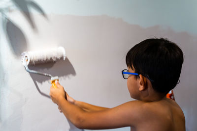 Repair in the apartment. happy child shirtless asian boy paints the wall with pastel pink paint.